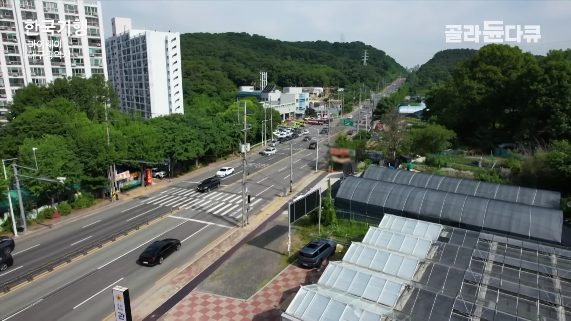 도심 외곽 도로와 인접한 비닐하우스 단지를 위에서 내려다본 항공 촬영 영상입니다.