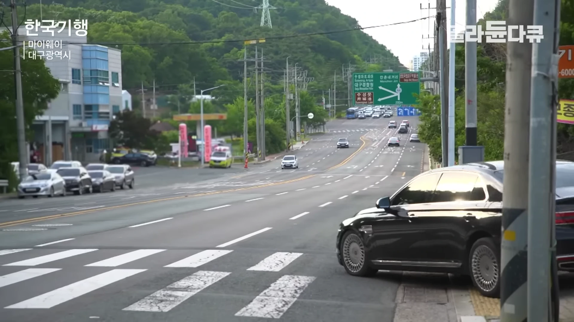 대구광역시의 한 도로에서 검은색 세단이 우측 정차 중이며, 전방으로 차량들이 달리는 도심 풍경이 보인다.