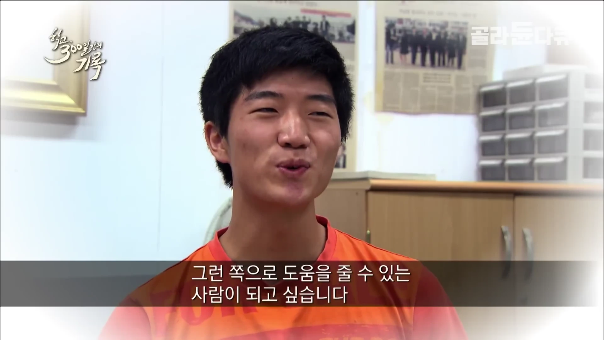 주황색 티셔츠를 입은 짧은 머리의 남학생이 실내에서 인터뷰하는 모습이며 하단 자막에는 '그런 쪽으로 도움을 줄 수 있는 사람이 되고 싶습니다'라는 문구가 적혀 있다.