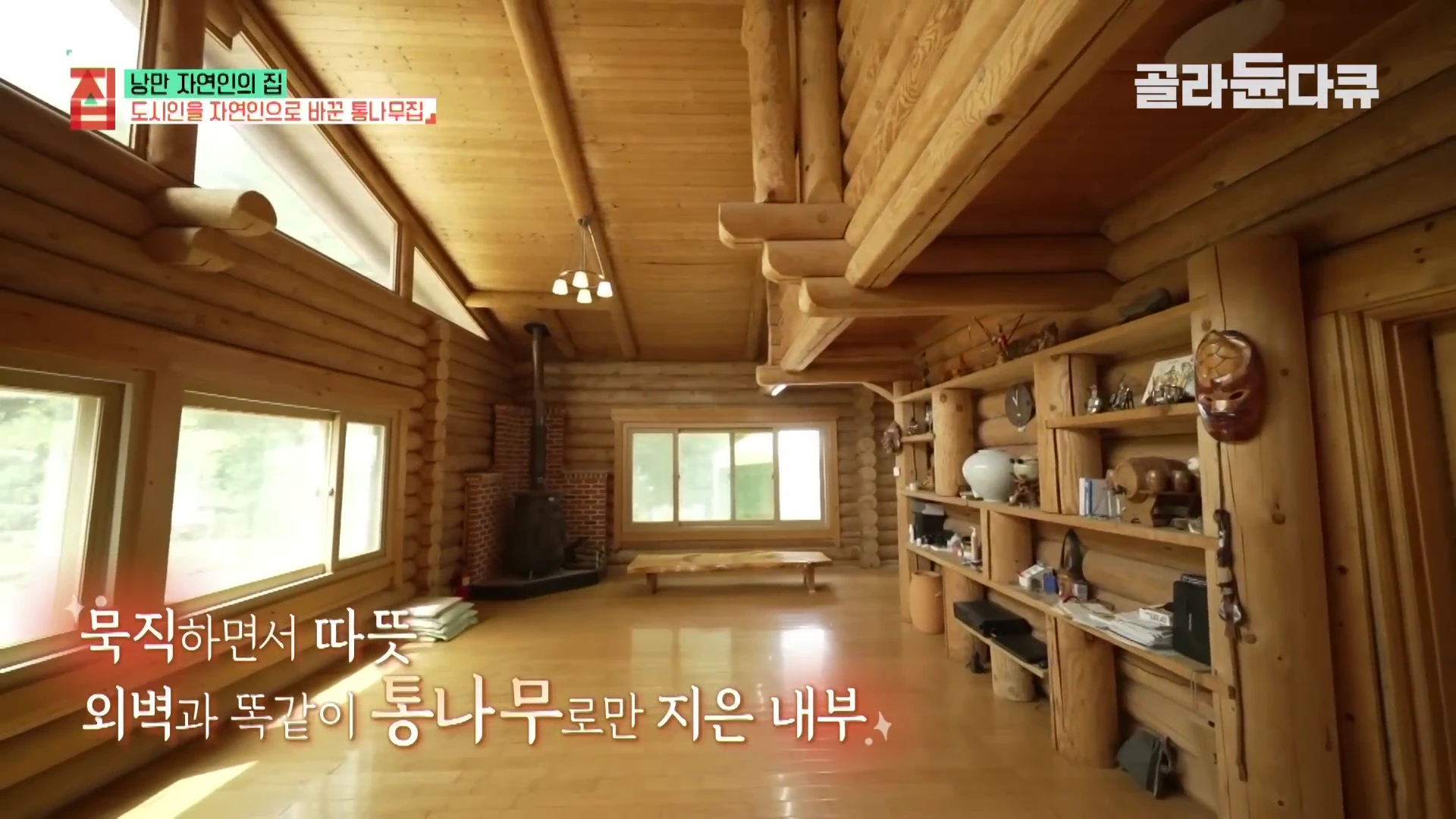 통나무로 마감된 넓은 거실의 내부 모습으로, 벽면과 천장이 나무로 되어 있으며 벽난로와 긴 수납 선반이 설치되어 있다.