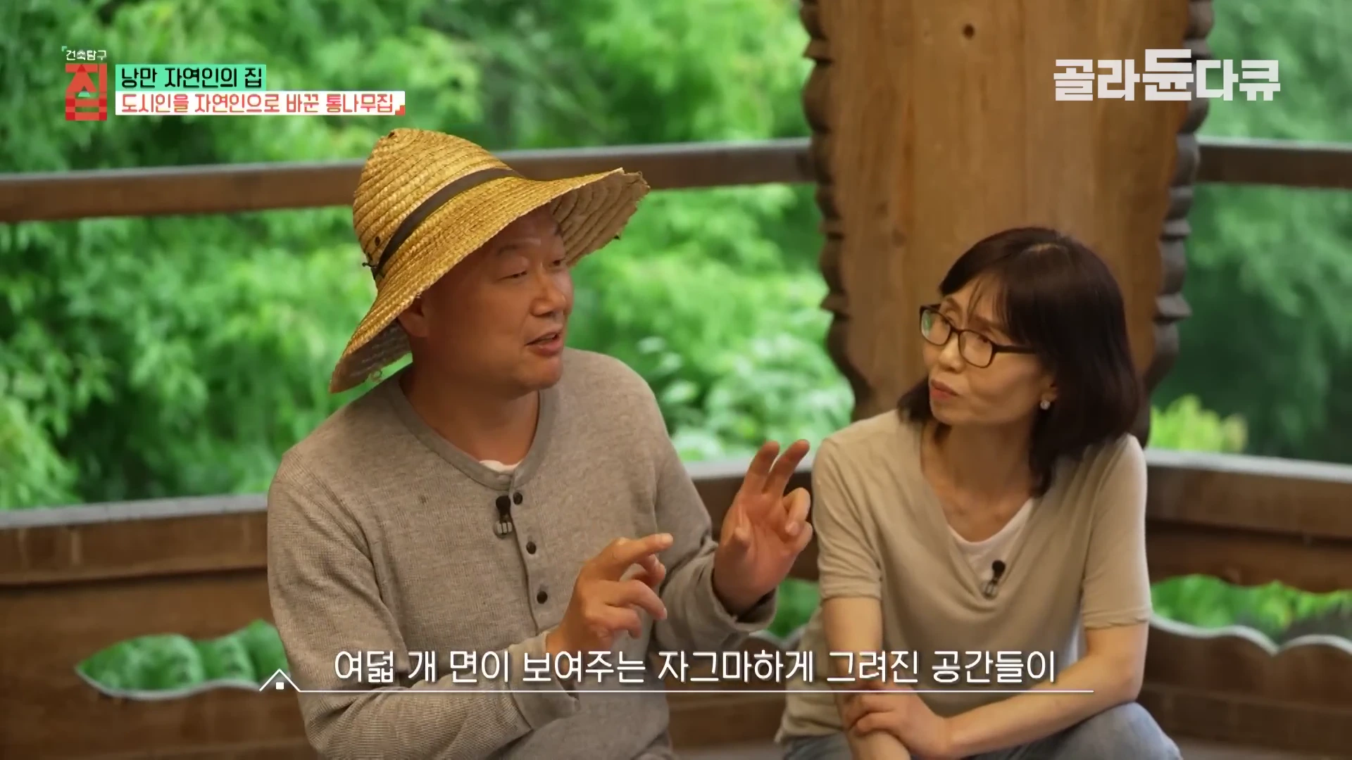 밀짚모자를 쓴 남성과 안경을 쓴 여성이 나무 기둥이 있는 정자 공간에서 대화를 나누고 있는 모습.