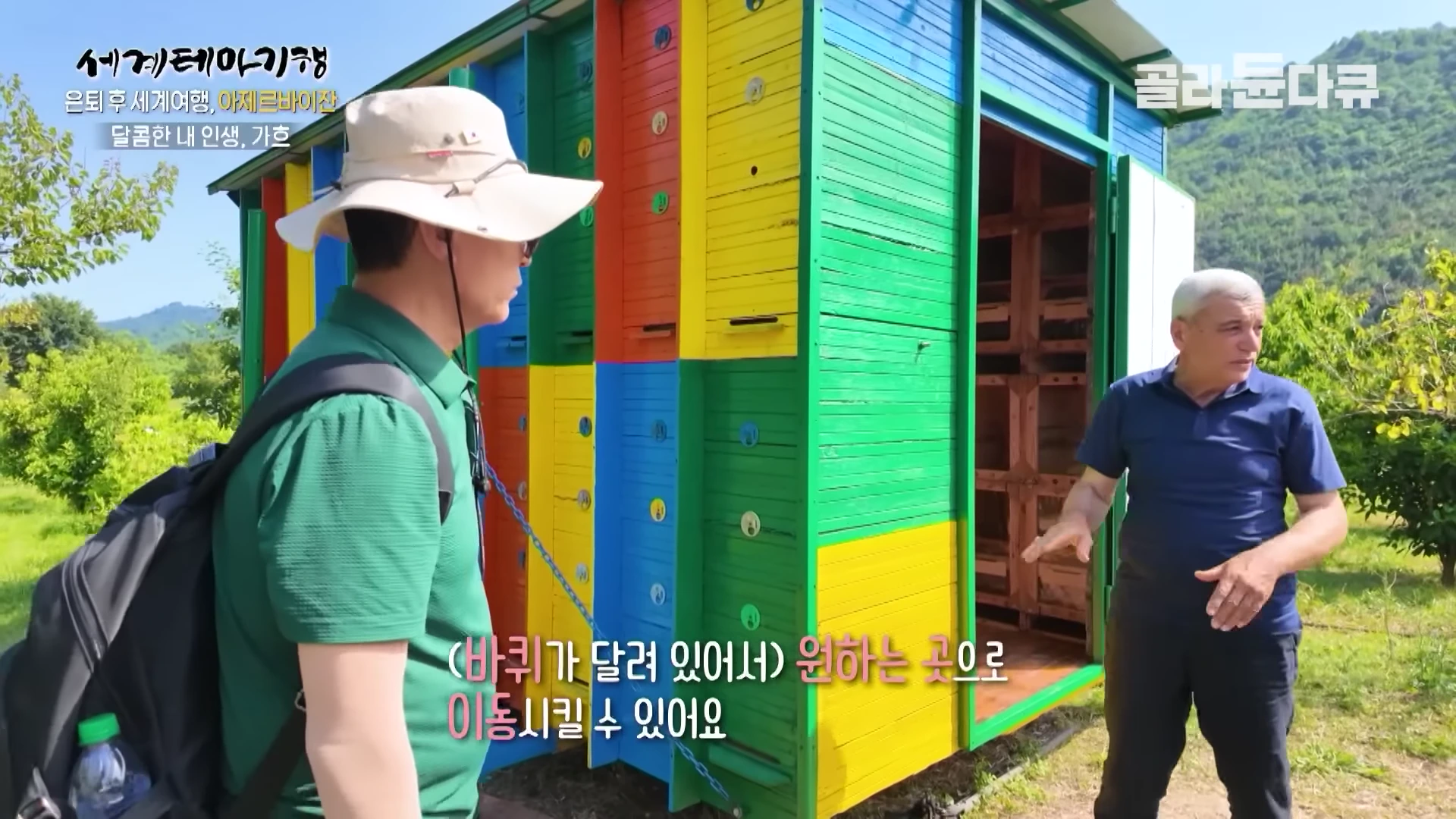 두 명의 남성이 알록달록하게 칠해진 이동식 벌집 컨테이너 앞에서 대화를 나누고 있는 모습