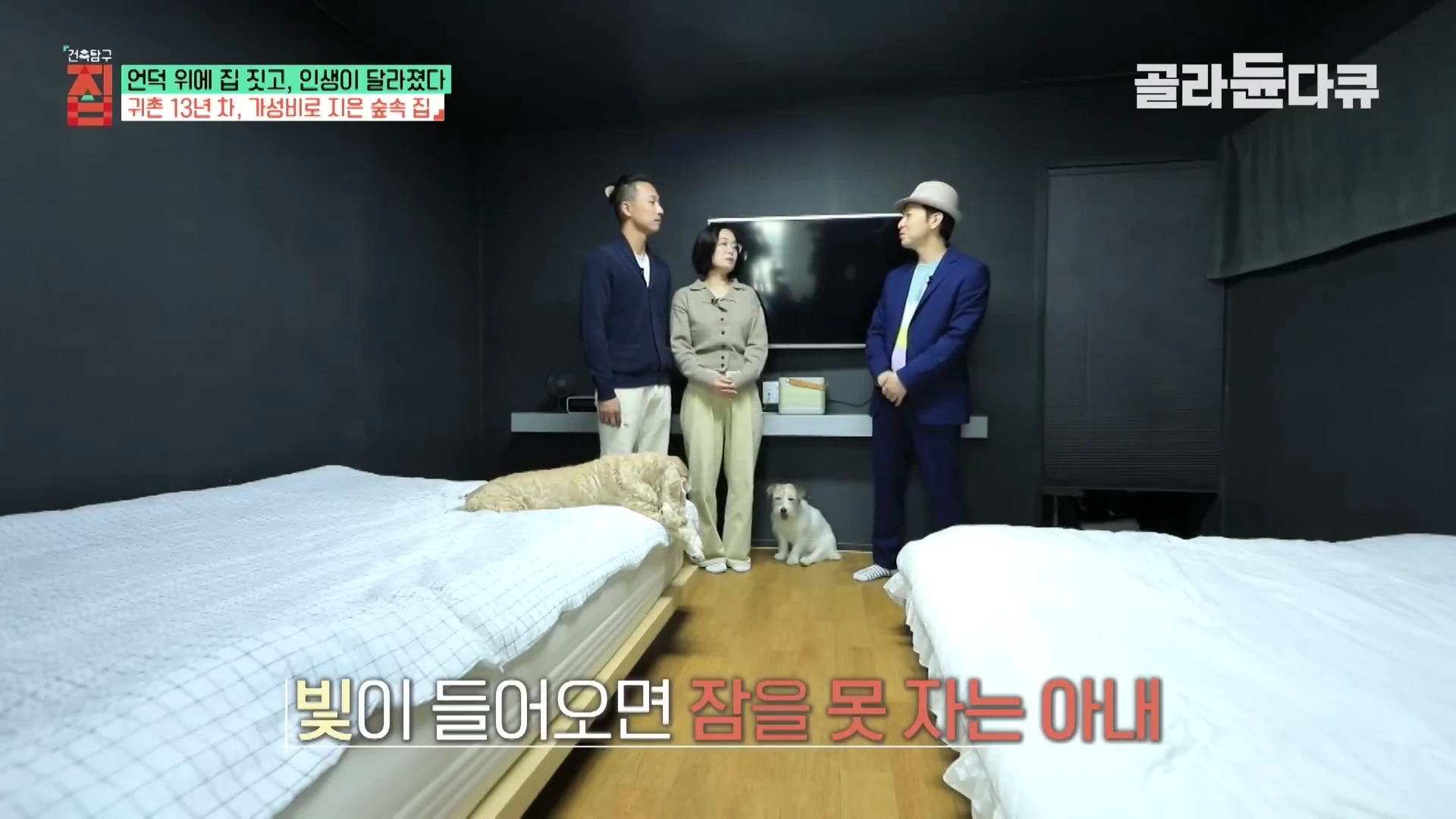 벽과 천장이 검은색으로 마감된 침실에 두 명의 출연자와 한 명의 진행자가 서 있고 그 옆에 반려견 두 마리가 있는 모습
