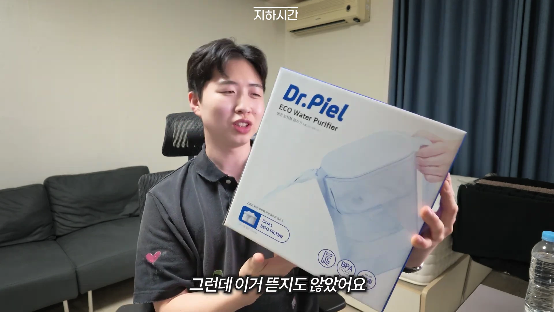 실내에서 한 남성이 닥터피엘 간이 정수기 상자를 양손으로 들어 보이고 있다.