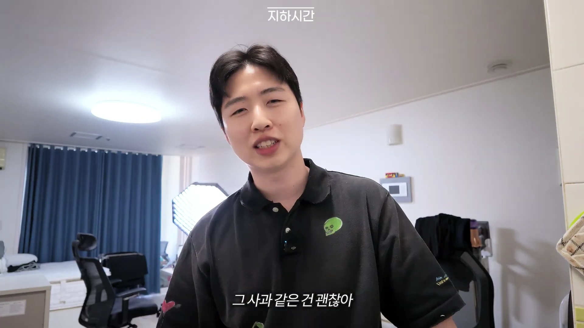 실내에서 검은색 피케 셔츠를 입은 남성이 카메라를 보며 이야기하고 있는 영상 화면