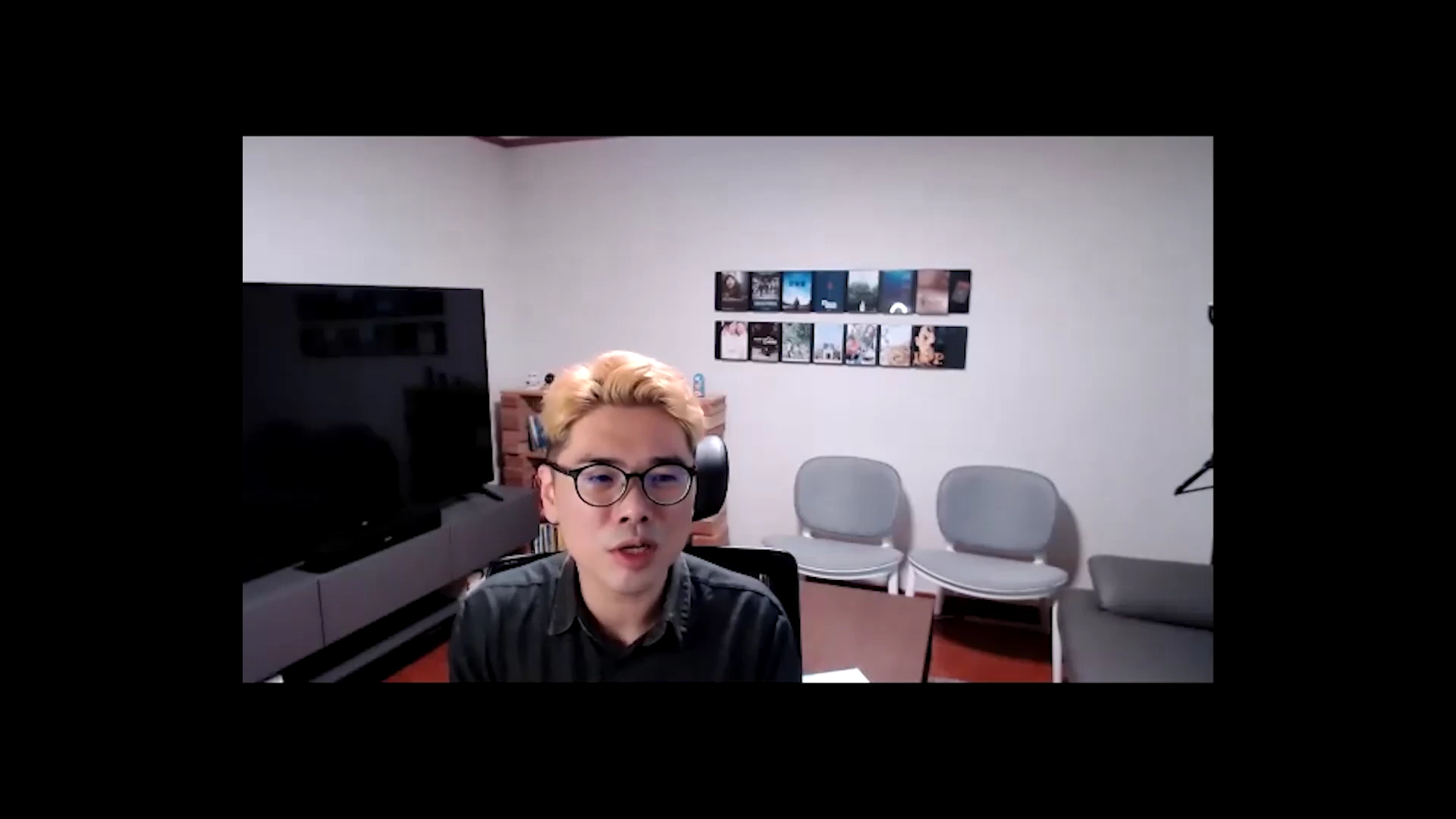밝은 탈색 머리에 안경을 쓴 남성이 실내에서 정면을 바라보며 이야기하고 있는 영상 화면입니다.