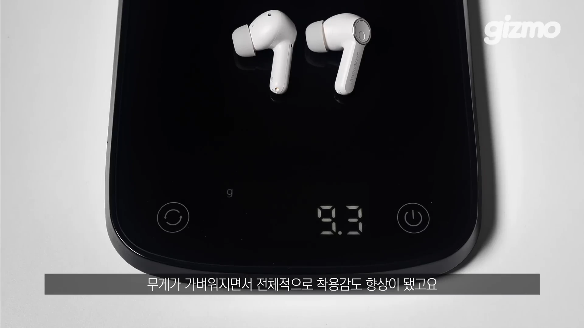 흰색 무선 이어폰 한 쌍이 검은색 디지털 저울 위에 놓여 있으며 화면에 9.3g이라는 무게가 표시되어 있습니다.