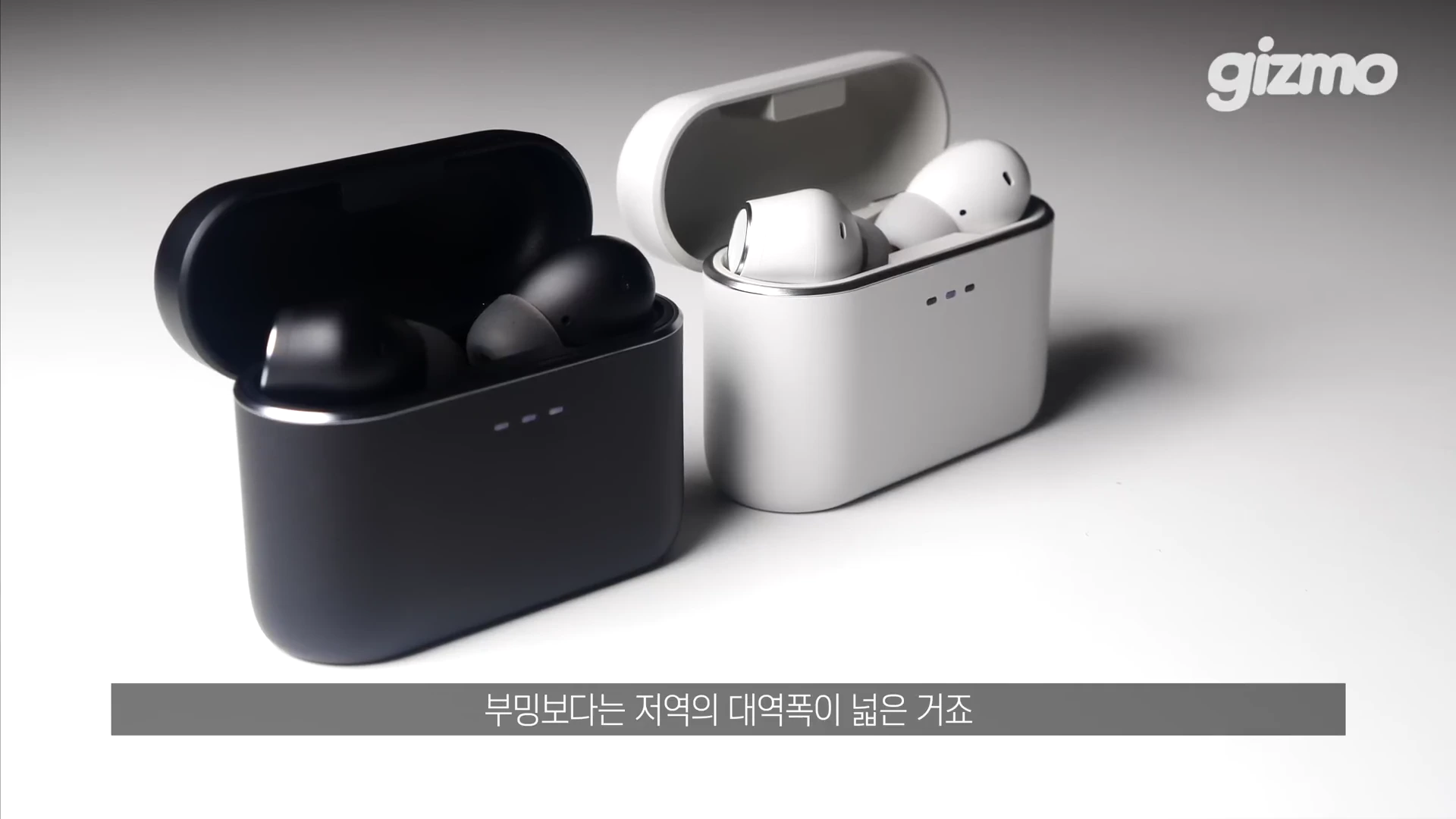 흰색과 검은색 무선 이어폰 충전 케이스가 나란히 놓여 있고, 하단에는 '부밍보다는 저역의 대역폭이 넓은 거죠'라는 자막이 표시된 화면.