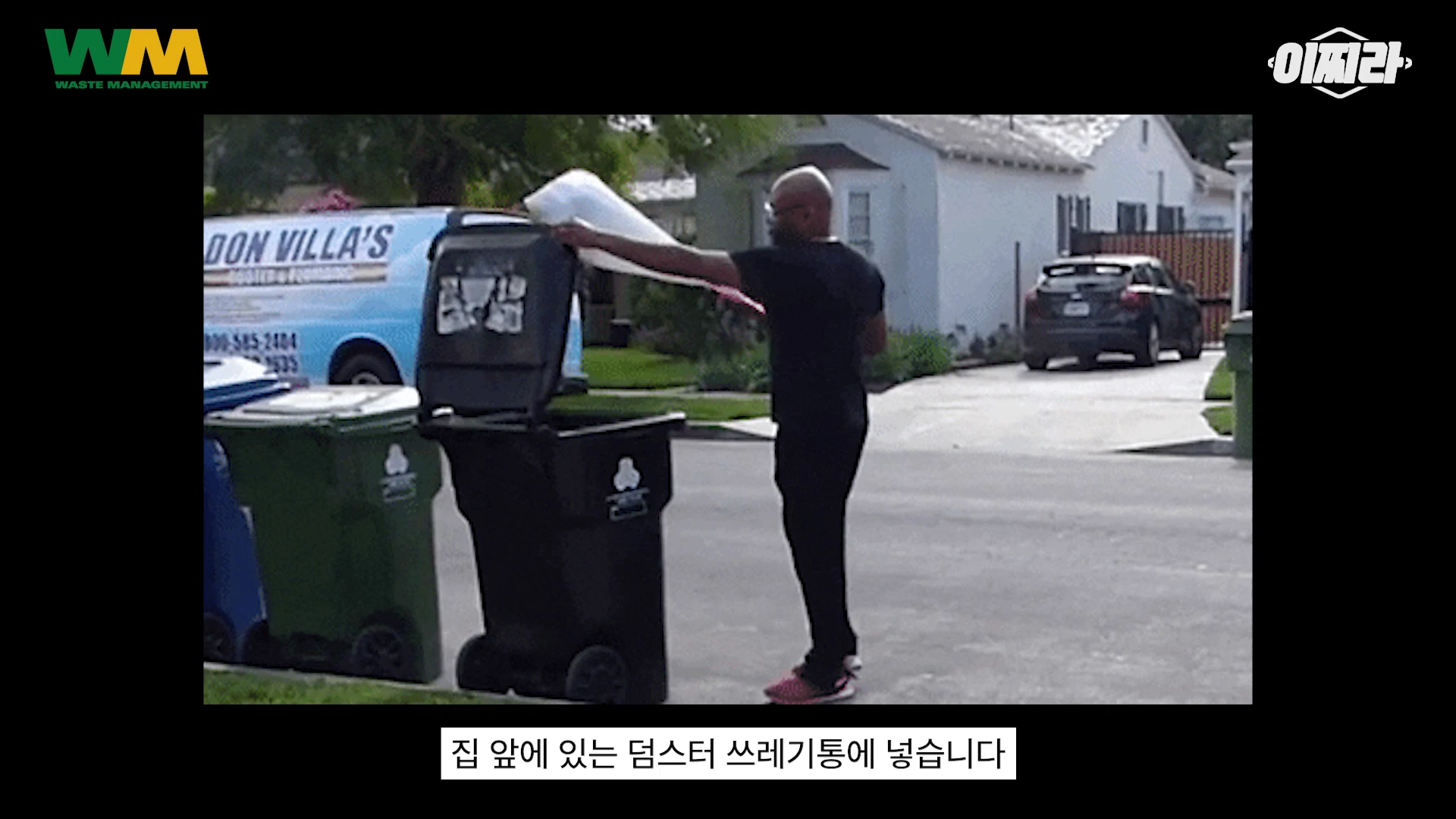 주택가 도로변에서 한 남성이 쓰레기 봉투를 들고 검은색 대형 쓰레기통에 넣고 있는 모습이 담긴 영상 캡처 화면입니다.