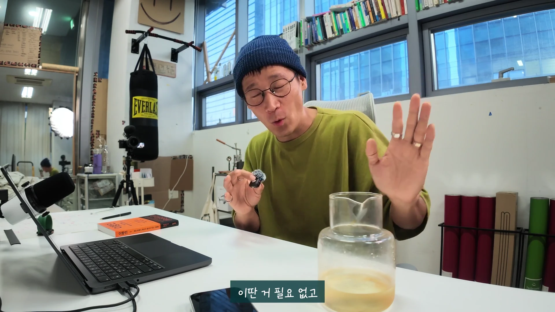 안경을 쓰고 비니를 쓴 남성이 책상 앞에 앉아 손짓하며 대화하는 모습이 담긴 영상 캡처 화면