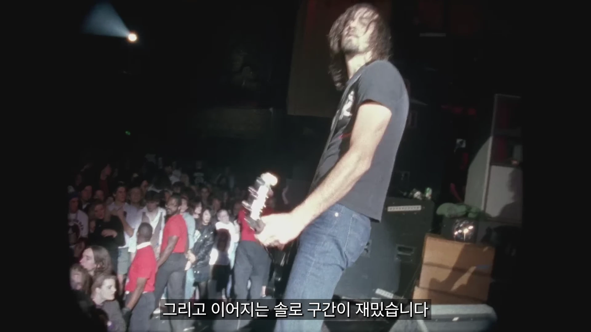 기타를 들고 있는 긴 머리의 남성이 어두운 공연장에서 관객들을 마주하며 서 있고, 아래쪽에는 한국어 자막이 표시되어 있습니다.