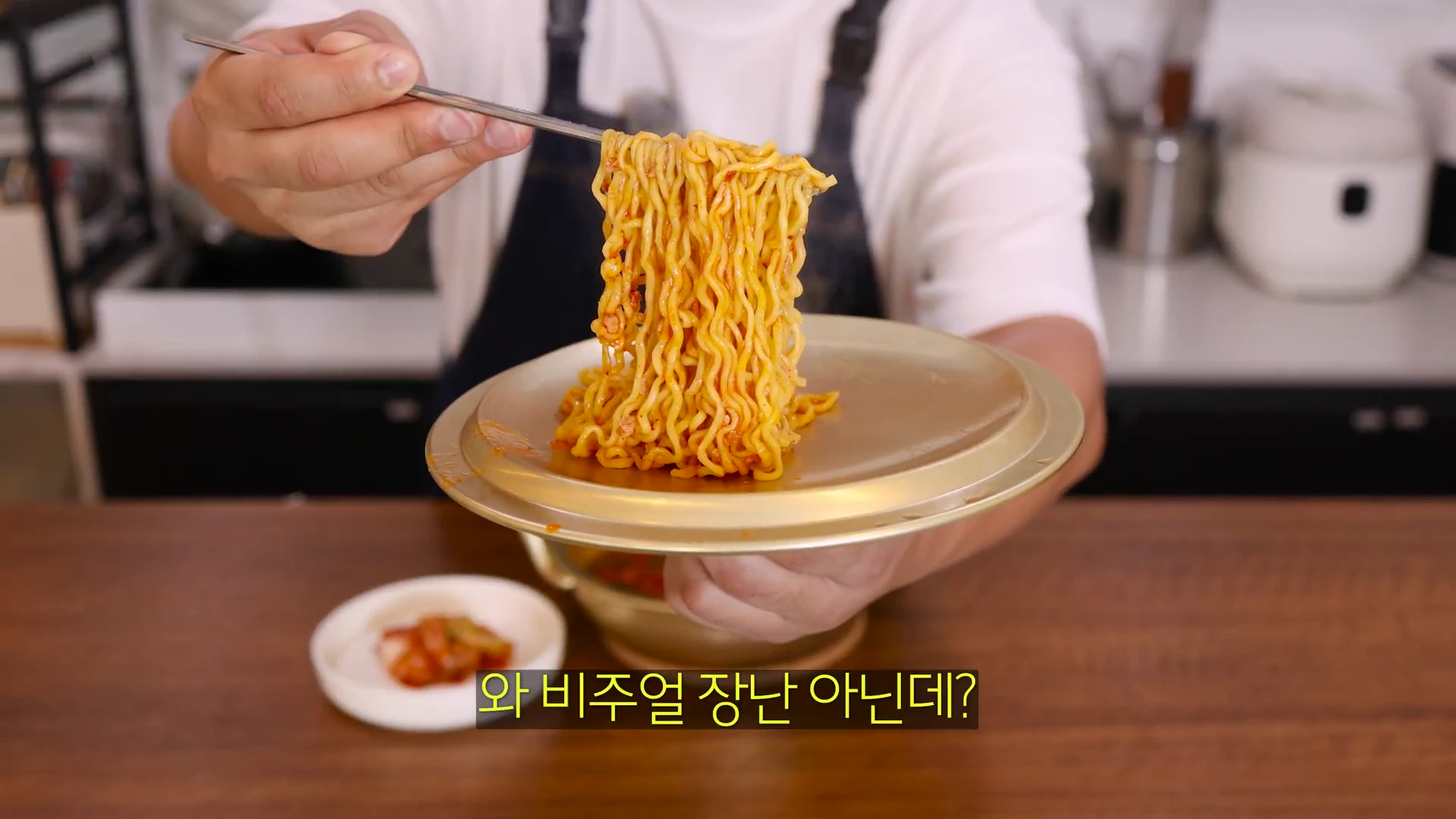흰색 반팔 티셔츠를 입은 요리사가 젓가락으로 갓 조리된 라면 면발을 들어 올리고 있으며, 화면 하단에는 '와 비주얼 장난 아닌데?'라는 자막이 적혀 있다.