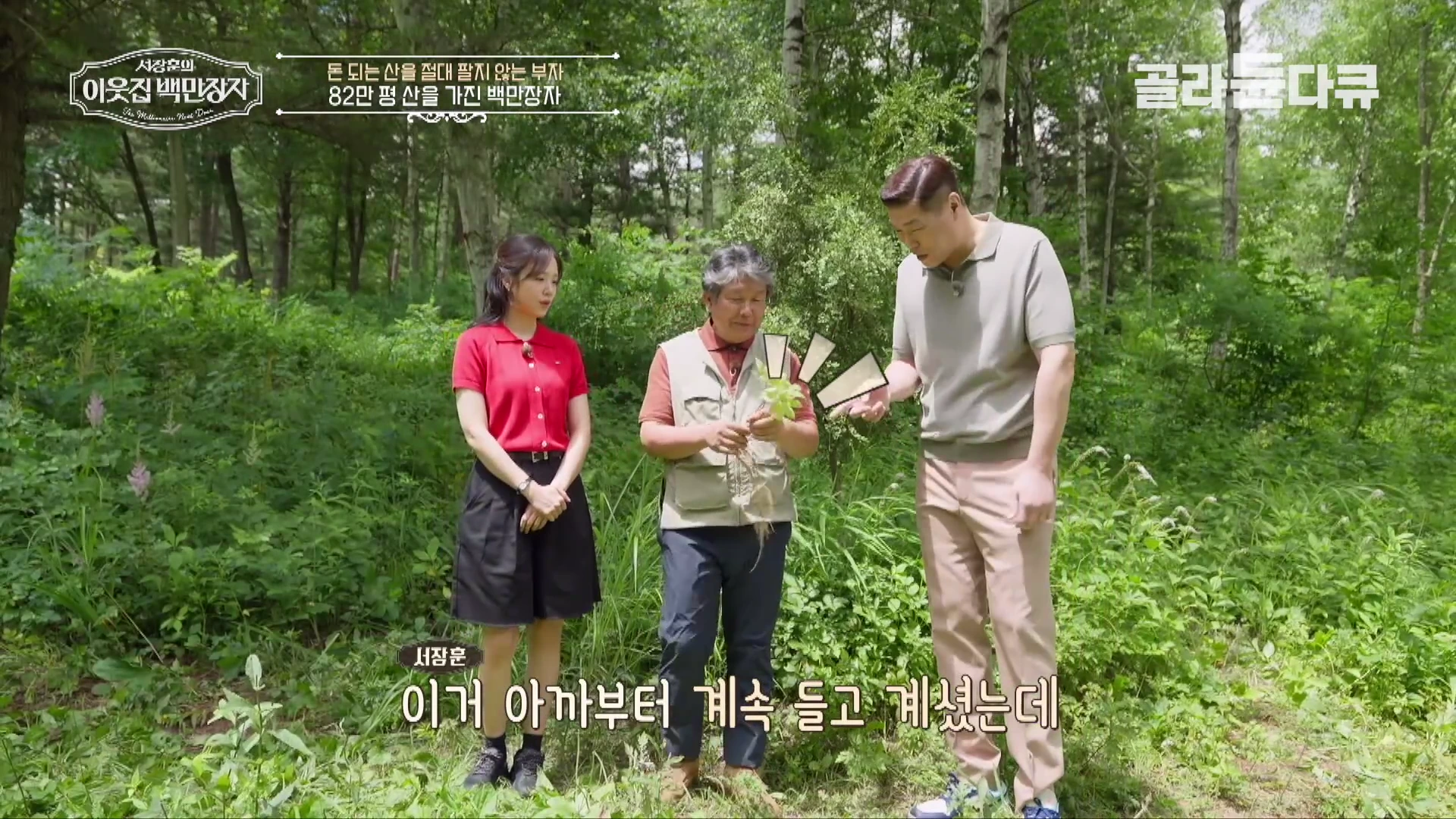 푸른 숲속에서 조끼를 입은 중년 남성이 손에 든 산삼을 서장훈과 한 여성에게 보여주고 있는 장면