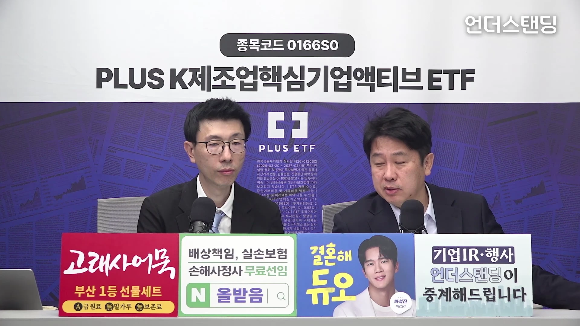 두 명의 남성이 검은 정장 차림으로 마이크 앞에 앉아 대화하고 있으며, 화면 상단에는 'PLUS K제조업핵심기업액티브 ETF' 문구가, 하단에는 여러 광고가 포함된 안내판이 배치되어 있습니다.