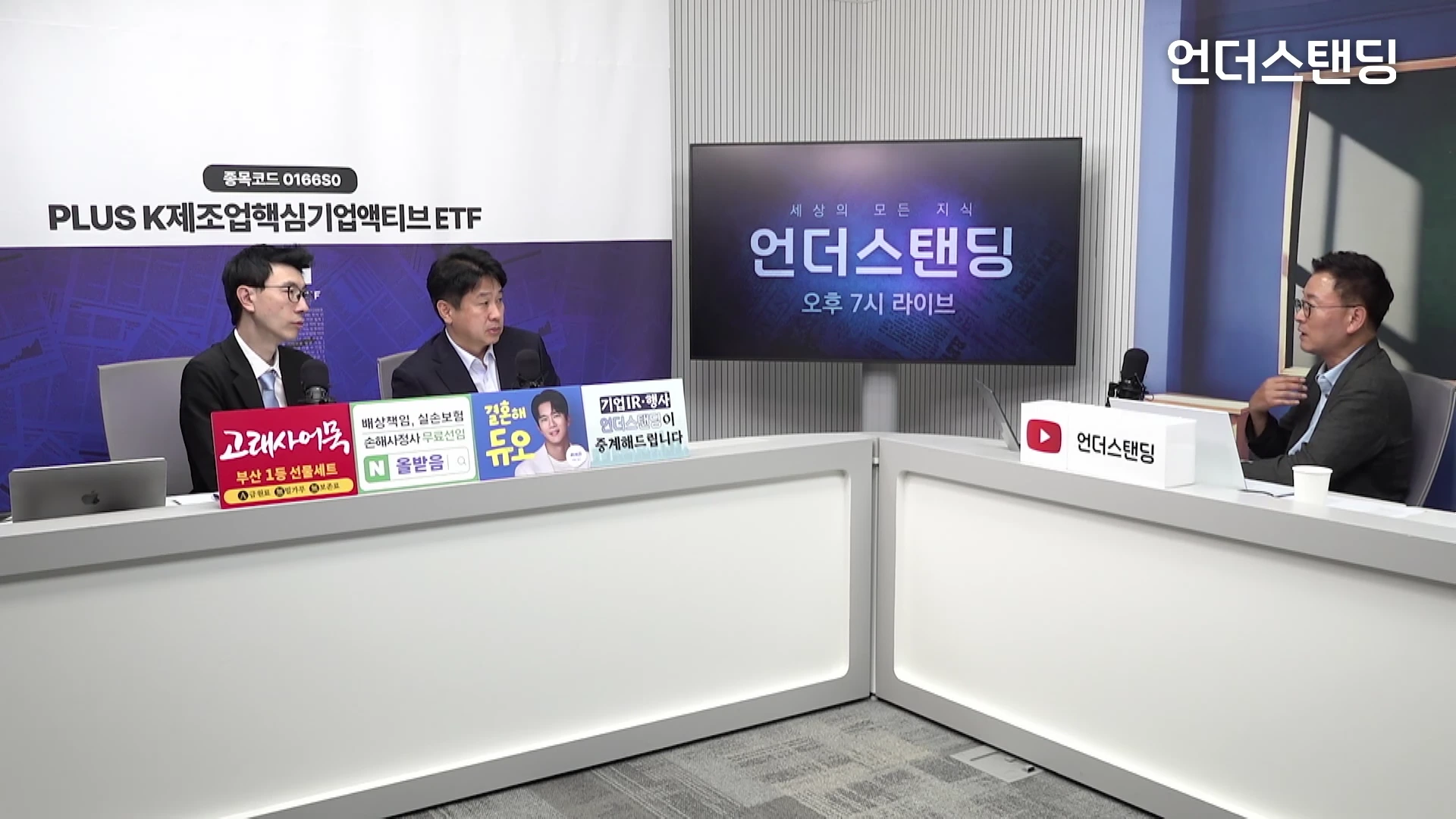 스튜디오에 세 명의 남성이 책상을 사이에 두고 앉아 마이크를 사용하며 대화를 나누고 있는 모습으로, 뒤편에는 로고가 새겨진 대형 화면이 배치되어 있습니다.