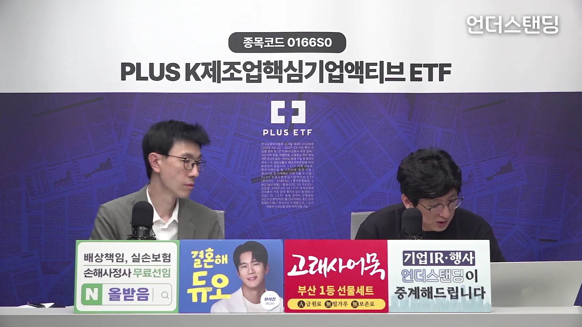 두 명의 남성이 스튜디오 책상 앞에 앉아 마이크를 사용해 대화하고 있으며, 앞쪽에는 광고 문구가 적힌 패널들이 나란히 놓여 있습니다.