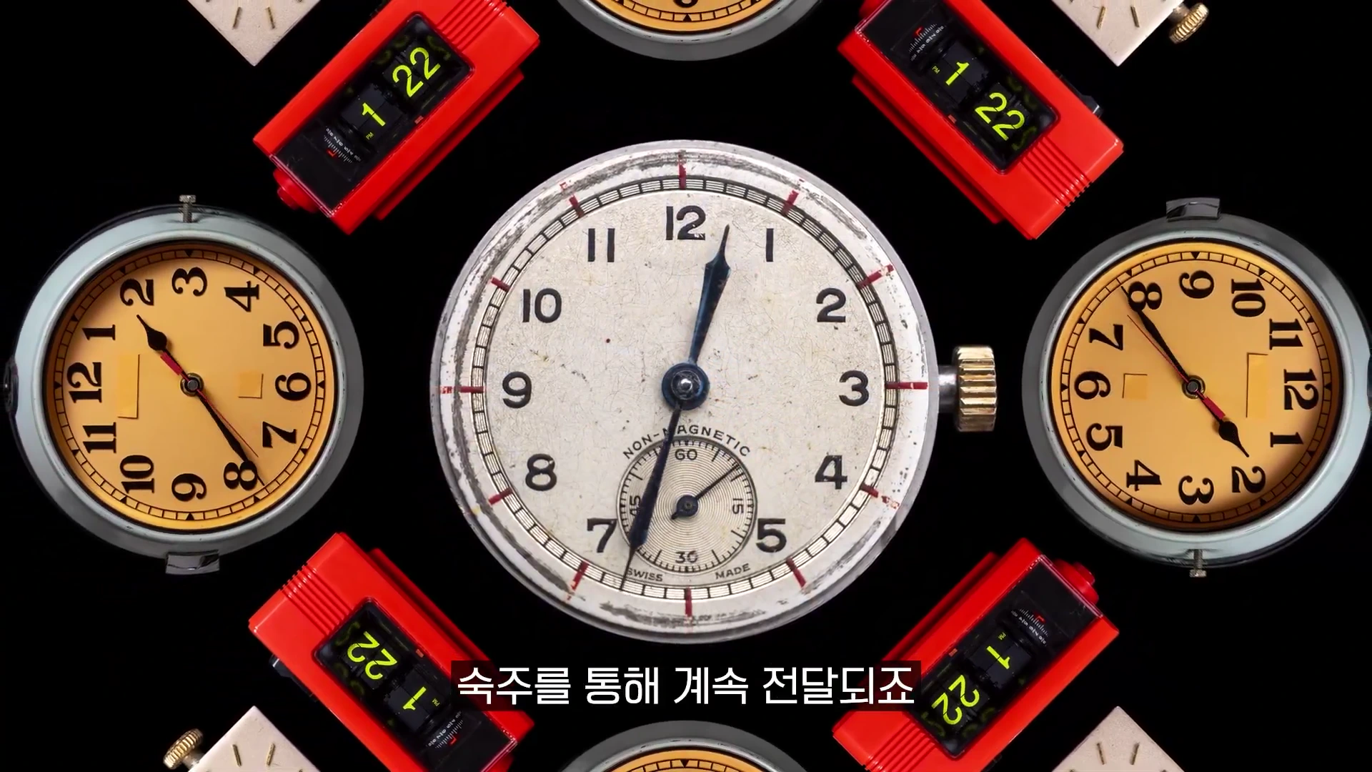 검은 배경 위에 여러 개의 아날로그 시계와 빨간색 디지털 시계가 원형으로 배치되어 있고 하단에는 한글 자막이 떠 있다.