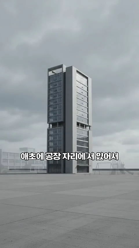 넓은 공터 중앙에 서 있는 현대적인 고층 건물 그래픽과 함께 '애초에 공장 자리에 서 있어서'라는 한국어 자막이 중앙에 적혀 있습니다.