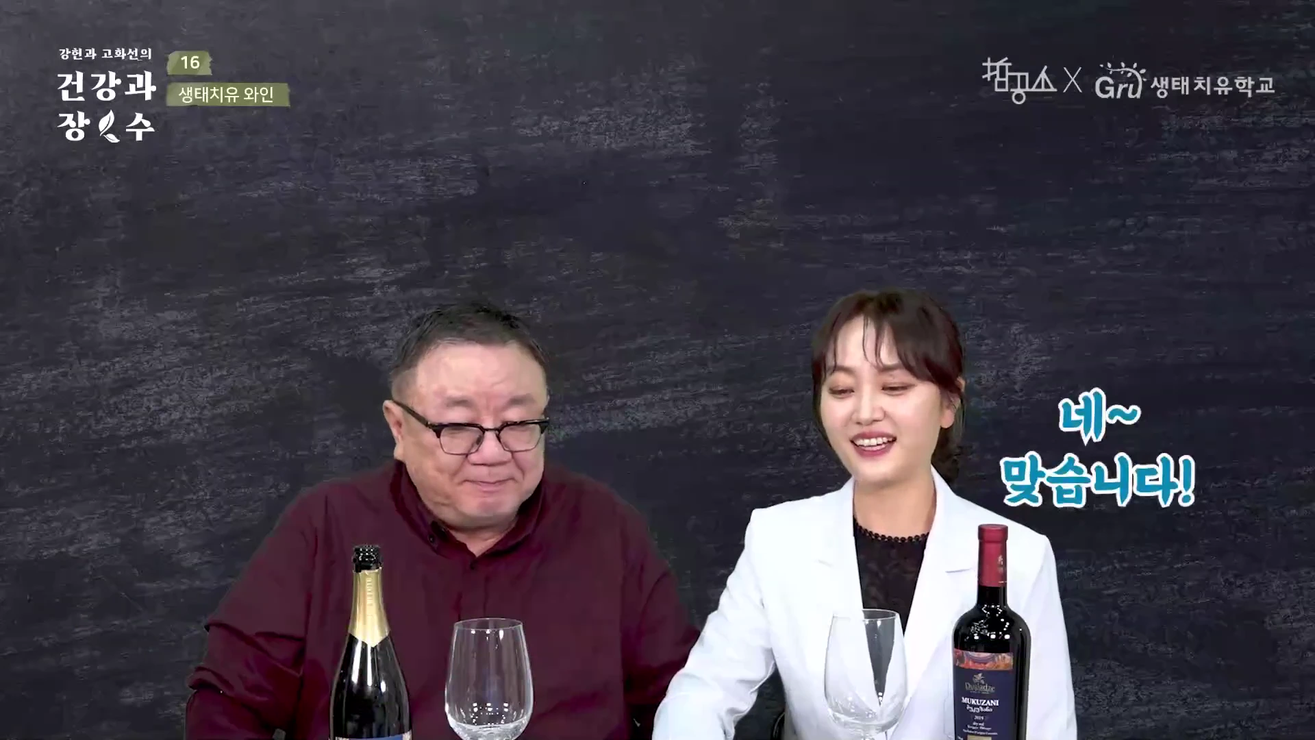 두 명의 출연자가 검은색 배경의 스튜디오에 앉아 있고, 앞 테이블에는 와인 병과 와인 잔이 놓여 있다. 화면 왼쪽 상단에는 프로그램 제목과 회차가 표시되어 있고, 오른쪽 상단에는 협력 기관 로고가 있다.