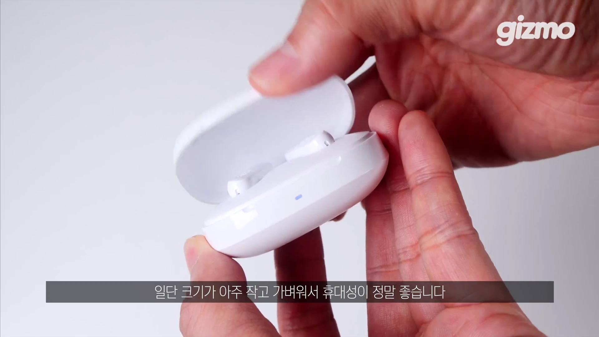 두 손으로 하얀색 무선 이어폰 충전 케이스를 열어 이어버드를 보여주는 모습.