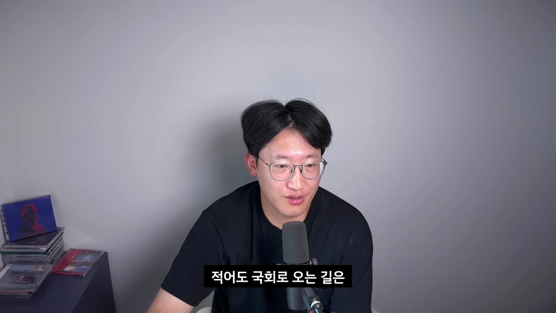 안경을 쓴 남성이 검은색 티셔츠를 입고 마이크 앞에서 이야기하고 있는 모습의 유튜브 영상 화면입니다.