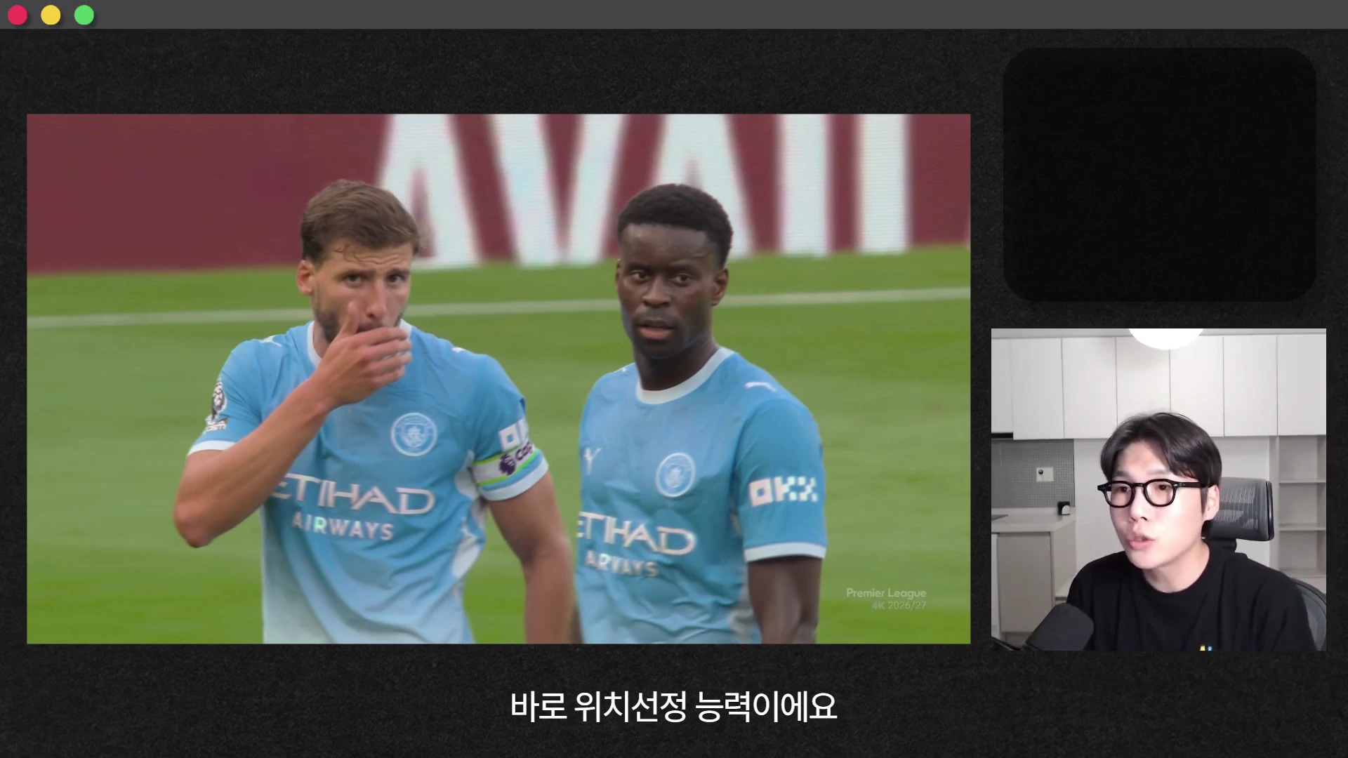 축구 경기 중 하늘색 유니폼을 입은 두 명의 선수와 화면 오른쪽 아래에 안경을 쓴 남성이 등장하는 영상 화면