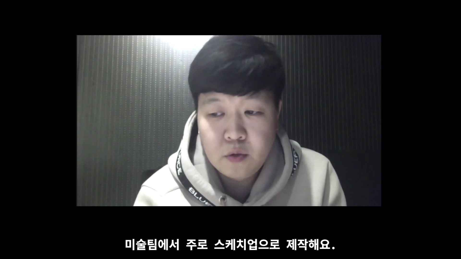 화상 인터뷰 화면에 검은 머리 남성이 후드티를 입고 앉아 있으며, 하단에는 '미술팀에서 주로 스케치업으로 제작해요.'라는 한국어 자막이 표시되어 있습니다.