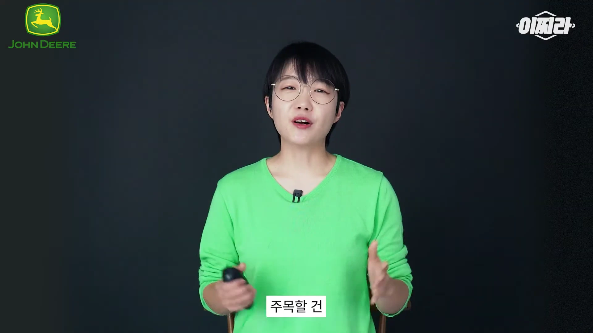 연두색 상의를 입고 안경을 쓴 진행자가 검은색 배경 앞에서 이야기하고 있다. 화면 상단에는 브랜드 로고와 콘텐츠 로고가 배치되어 있고 하단에는 자막이 떠 있다.