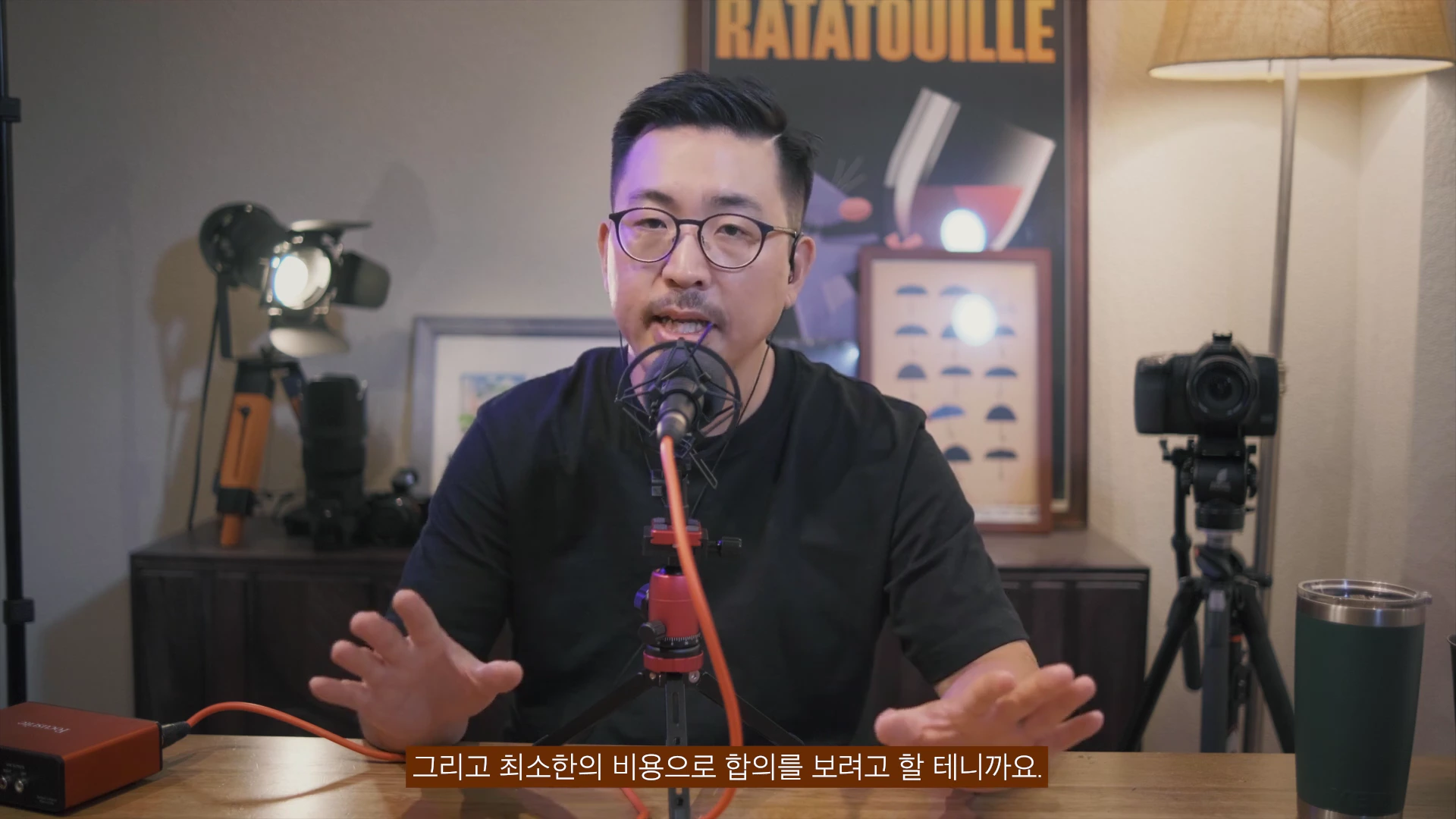 안경을 쓴 남성이 마이크 앞에 앉아 손짓을 하며 이야기를 하고 있는 스튜디오 모습