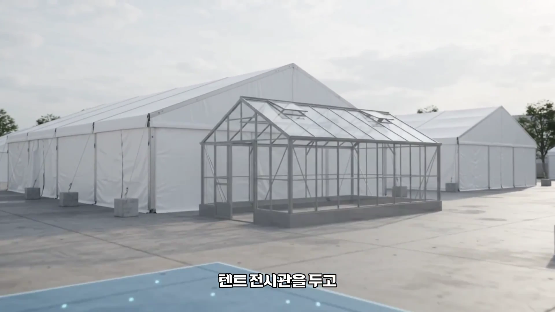 흰색 대형 임시 천막들과 투명한 유리 온실 형태의 구조물이 넓은 광장에 설치되어 있는 모습