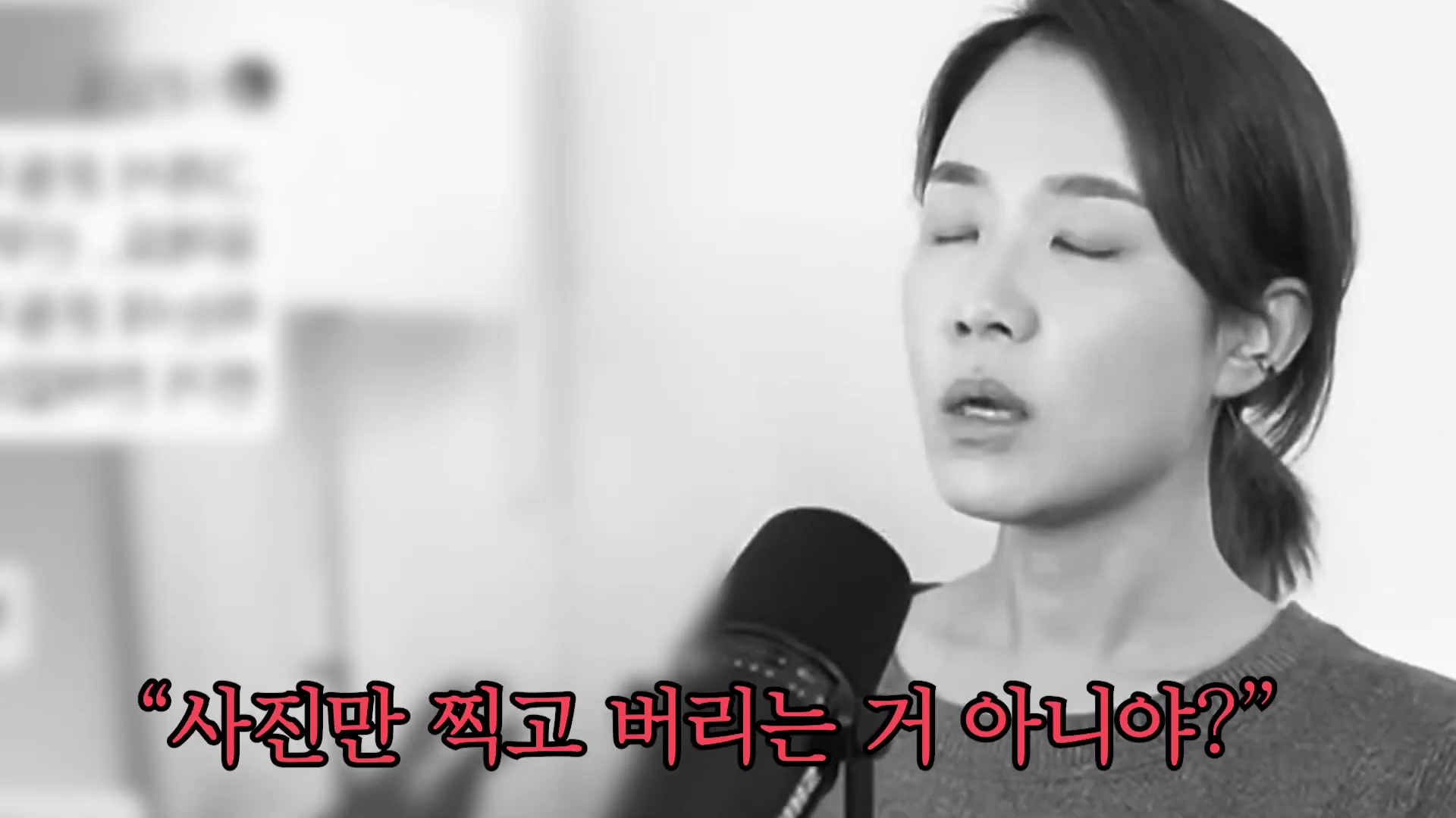 마이크 앞에 선 여성이 눈을 감고 이야기를 하고 있으며, 하단에는