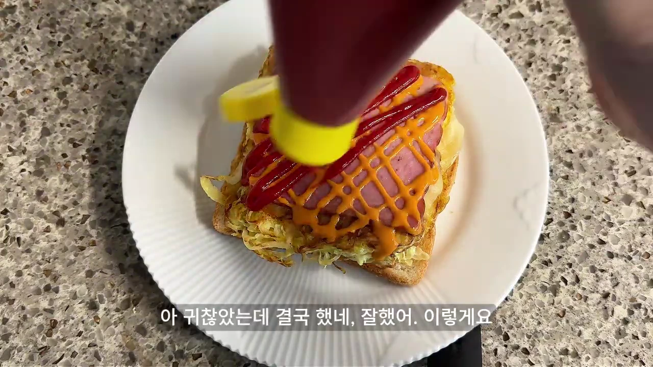흰색 접시 위에 놓인 토스트에 노란색과 빨간색 소스를 뿌리는 모습이 위에서 아래로 촬영되어 있다.