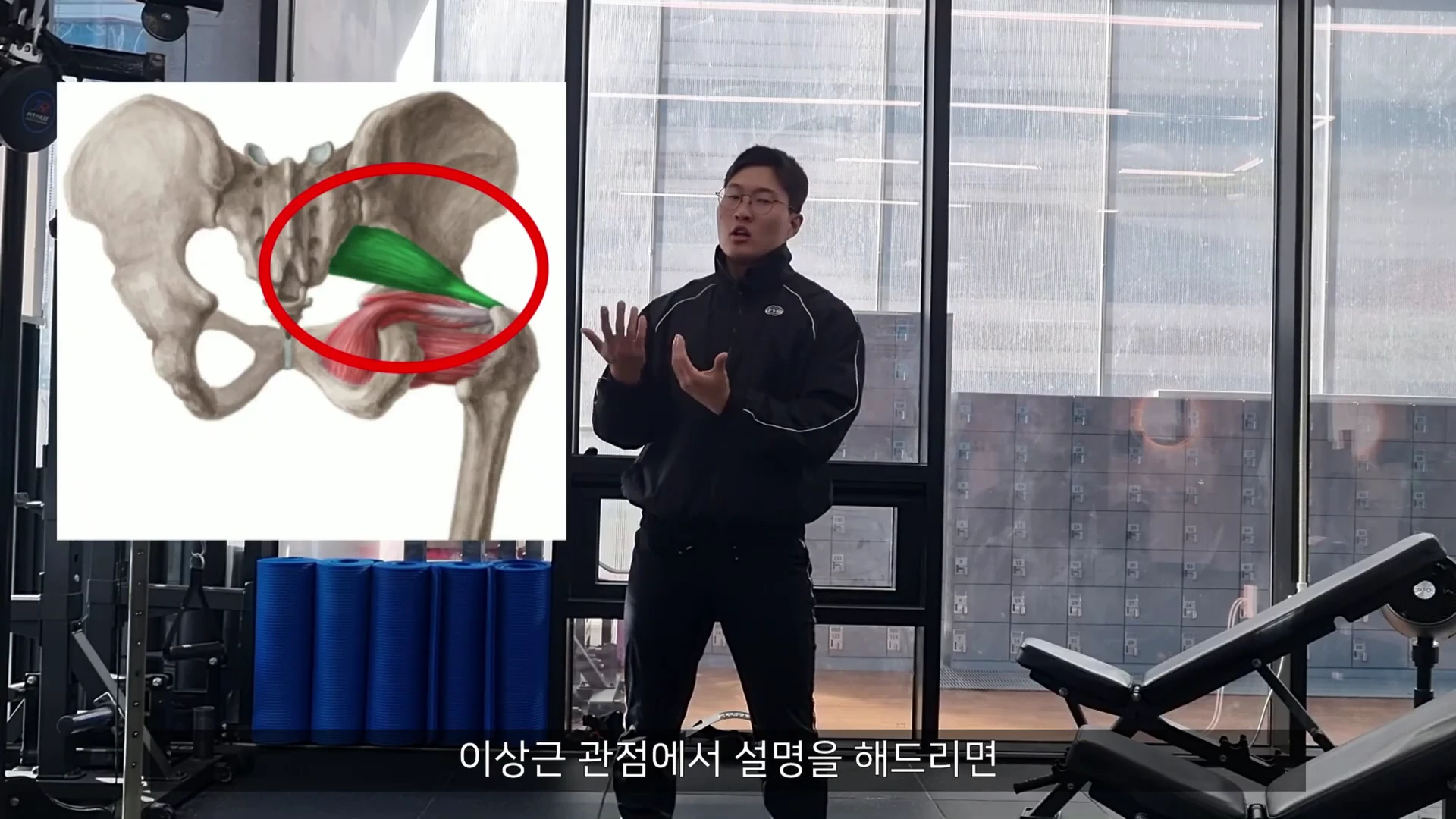 피트니스 센터에서 운동복을 입은 남성이 서서 설명하고 있으며, 화면 왼쪽에는 골반 뼈와 이상근을 강조한 해부학 그래픽이 삽입되어 있다.