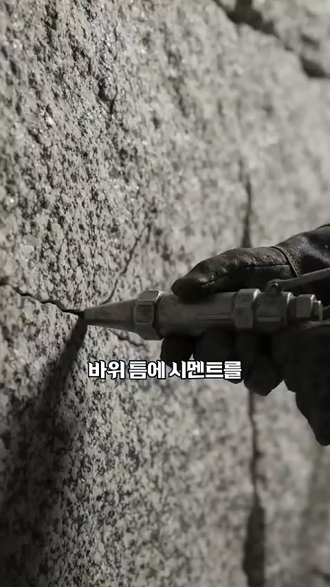 장갑을 낀 손이 노즐을 사용하여 바위 틈에 시멘트를 주입하고 있는 모습