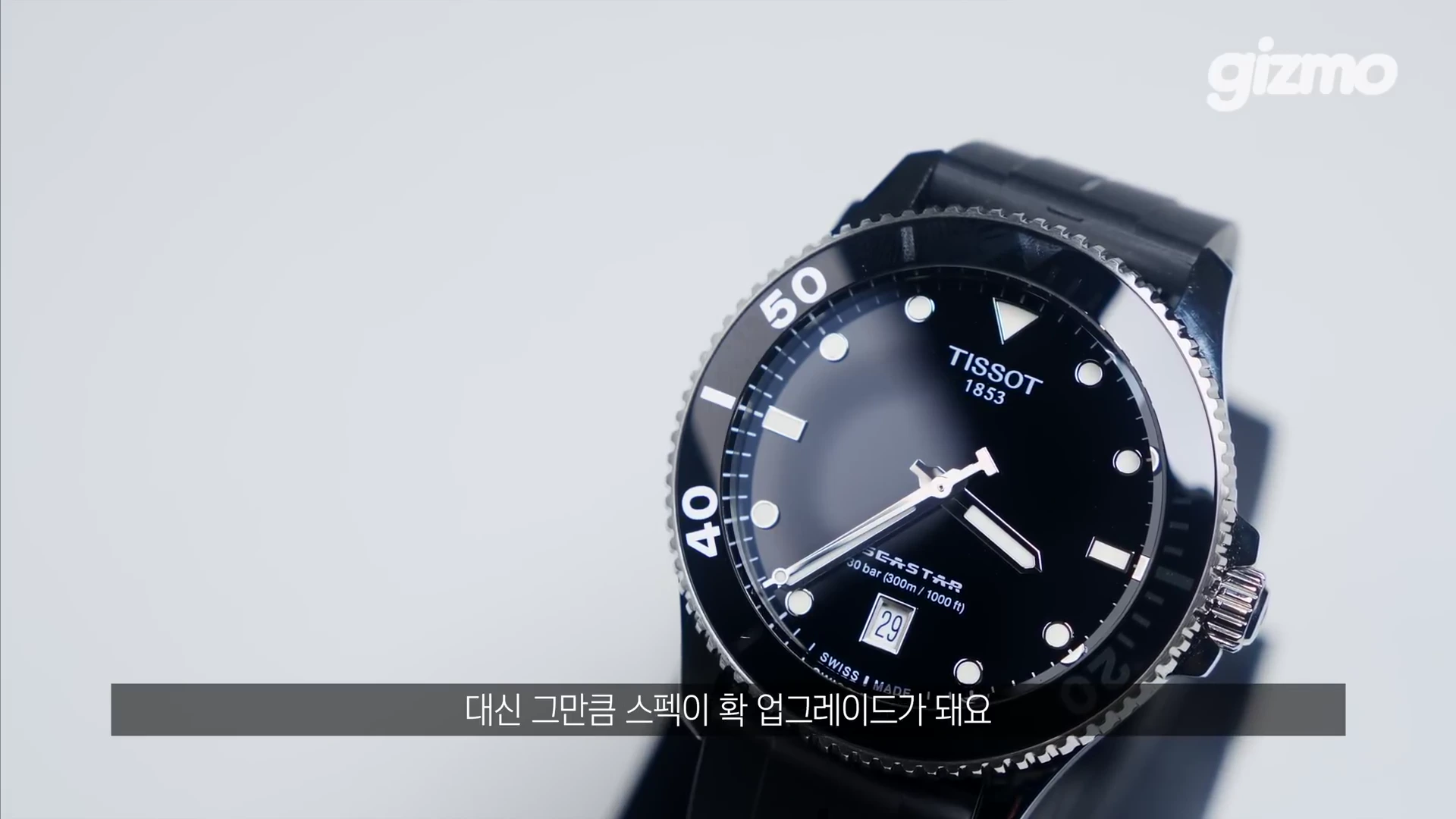 검은색 다이얼과 베젤을 갖춘 티쏘 씨스타 1000 다이버 워치가 흰색 배경 위에 놓여 있고, 하단에는 자막이 포함되어 있습니다.