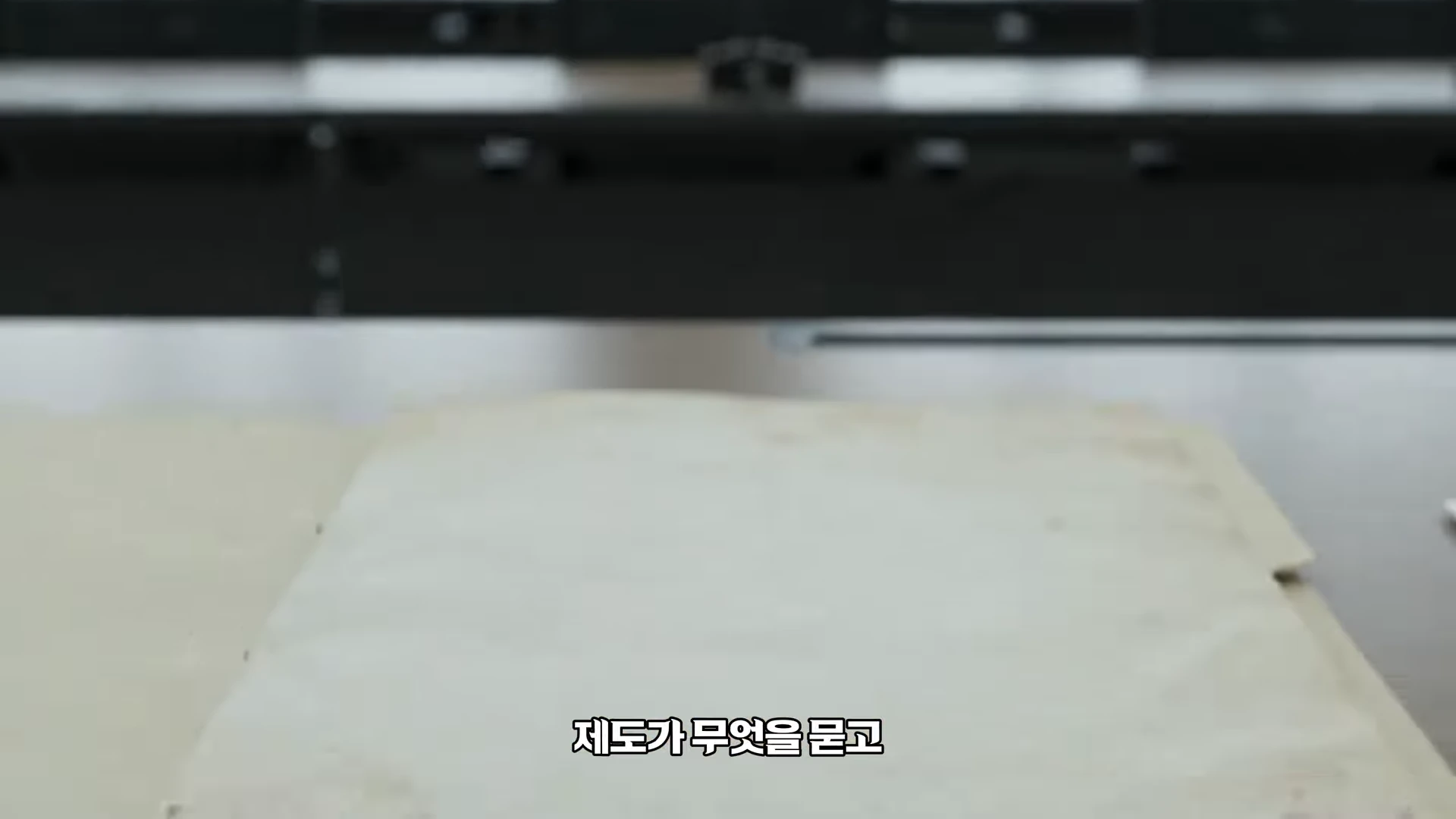 탁자 위에 놓인 낡고 누런 서류 뭉치와 그 아래 위치한 '제도가 무엇을 묻고'라는 자막이 겹쳐진 화면