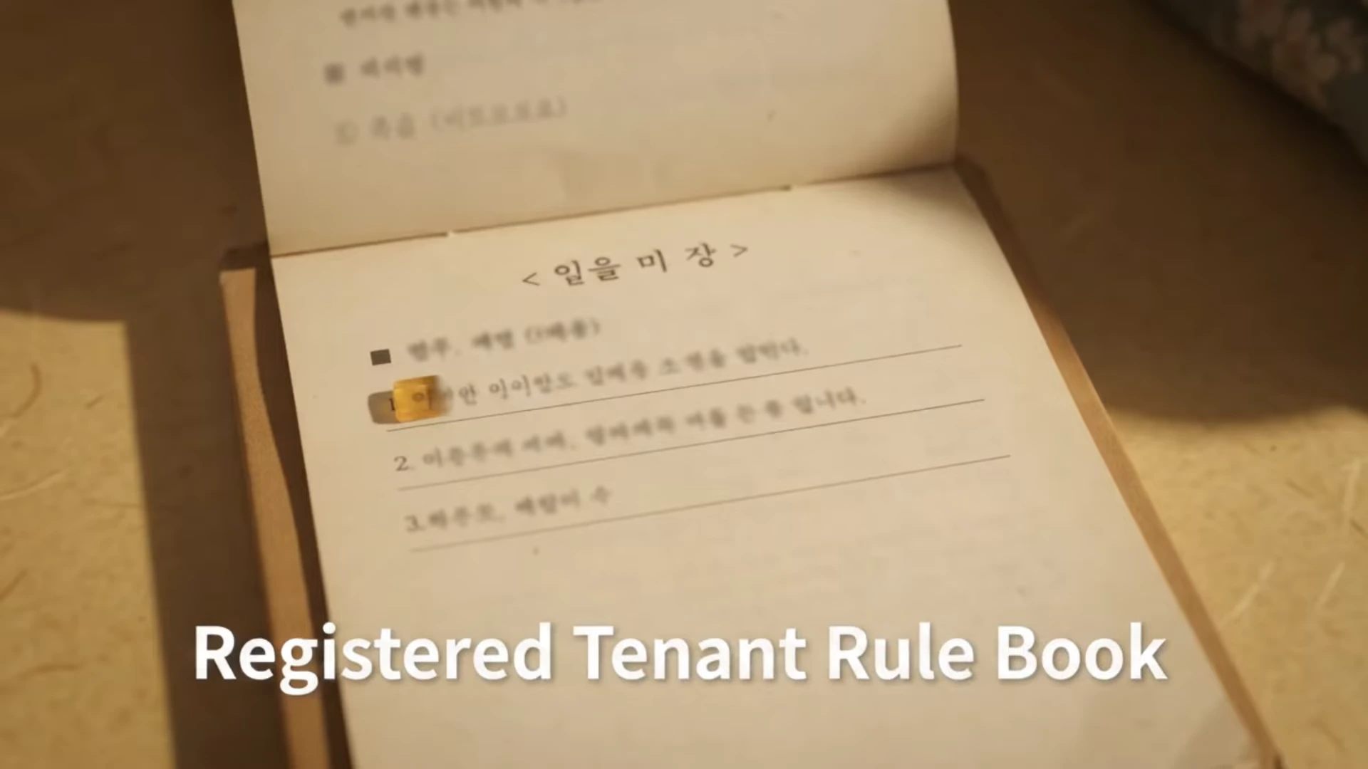 펼쳐진 오래된 종이 문서에는 '일을 미장'이라는 제목과 함께 임대 관련 항목들이 적혀 있고, 하단에는 'Registered Tenant Rule Book'이라는 문구가 영문으로 덧붙여져 있다.