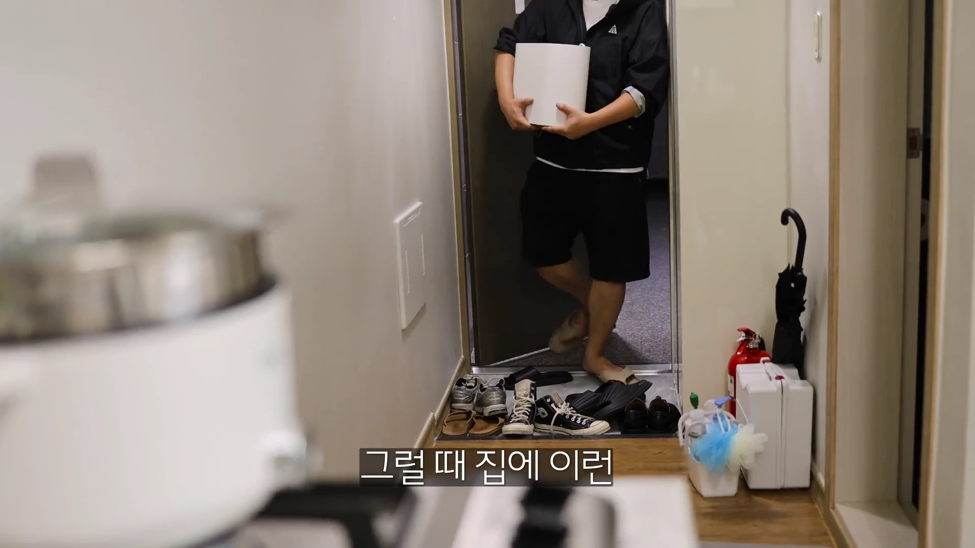 흰색 원통형 물건을 양손으로 들고 현관문을 통해 실내로 들어오는 남성의 모습.