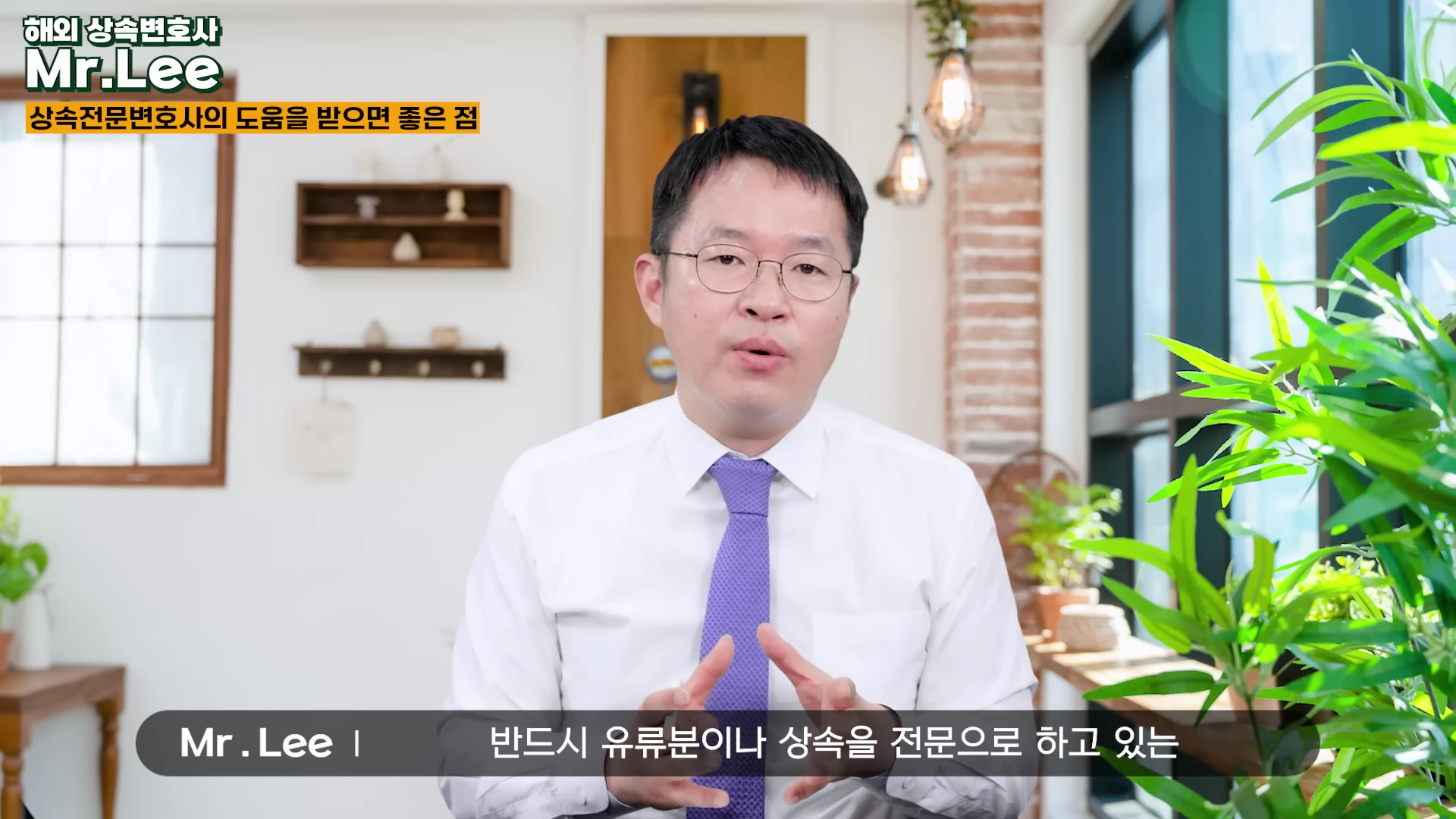 흰 셔츠에 보라색 넥타이를 맨 안경 쓴 남성이 밝은 실내에서 정면을 응시하며 이야기하고 있는 모습.