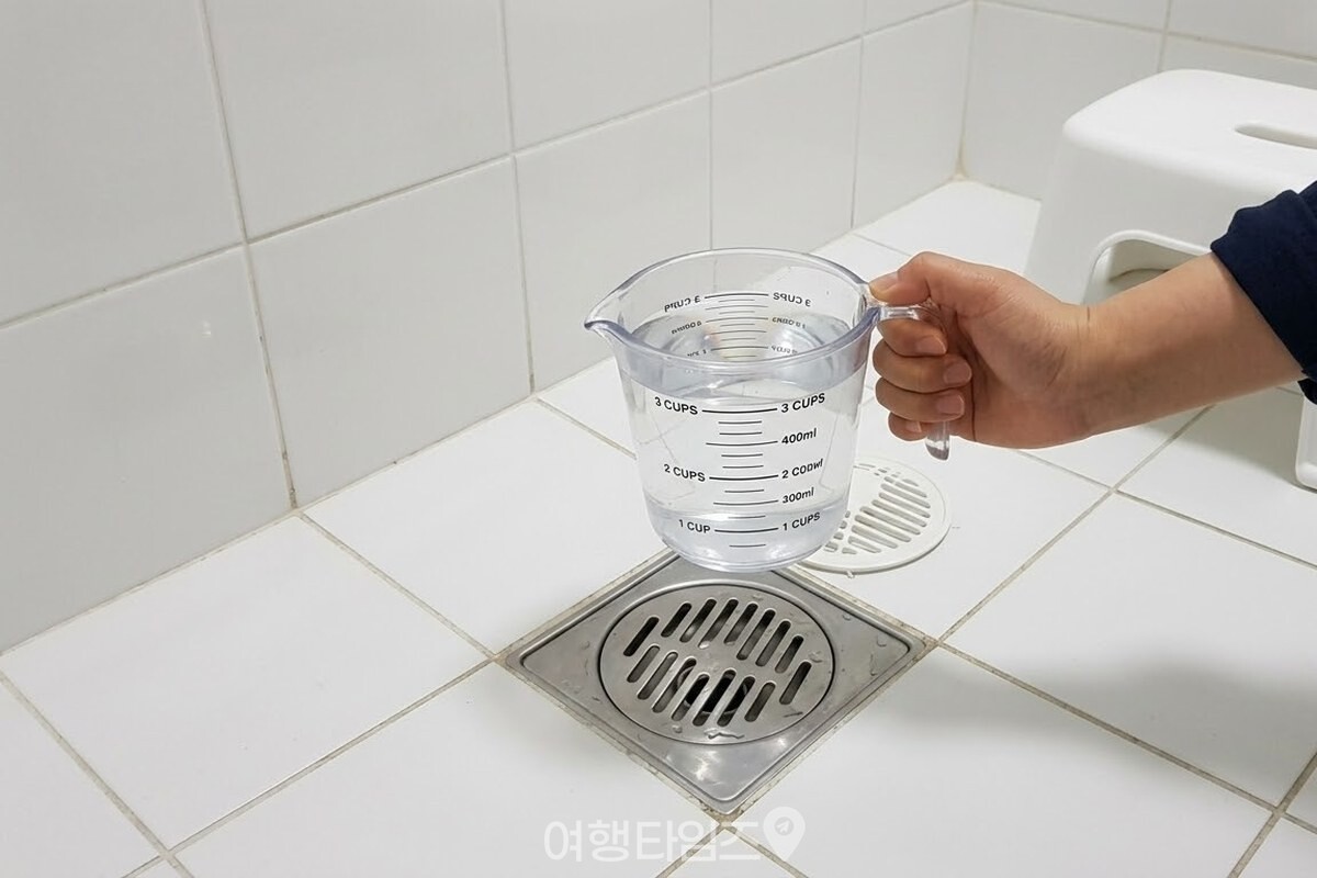 물 두 컵을 담은 투명 계량컵을 손에 들고 배수구 앞에 서 있다. / 기사 이해를 돕기 위한 생성형 이미지