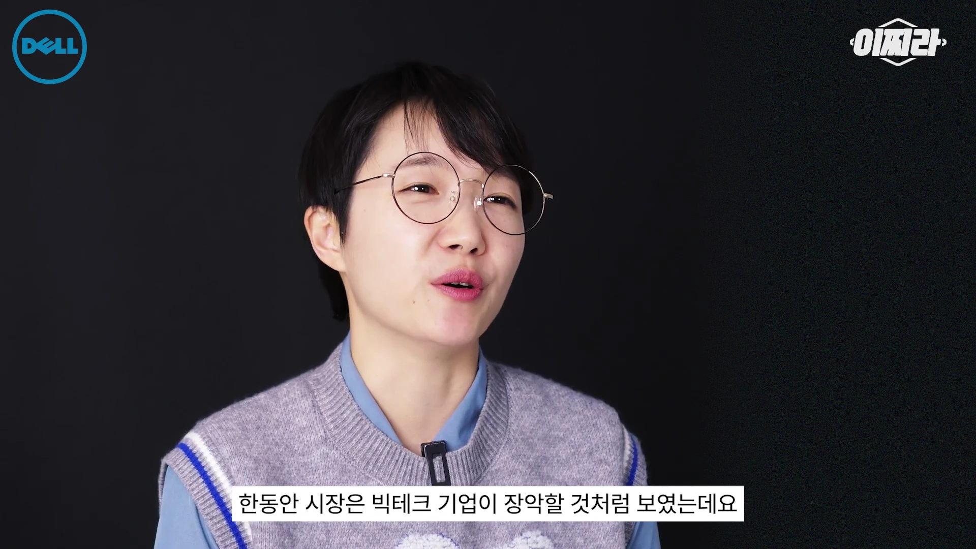 안경을 쓴 단발머리의 여성이 검은색 배경 앞에서 이야기하고 있으며 화면 하단에는 자막이 달려 있다.