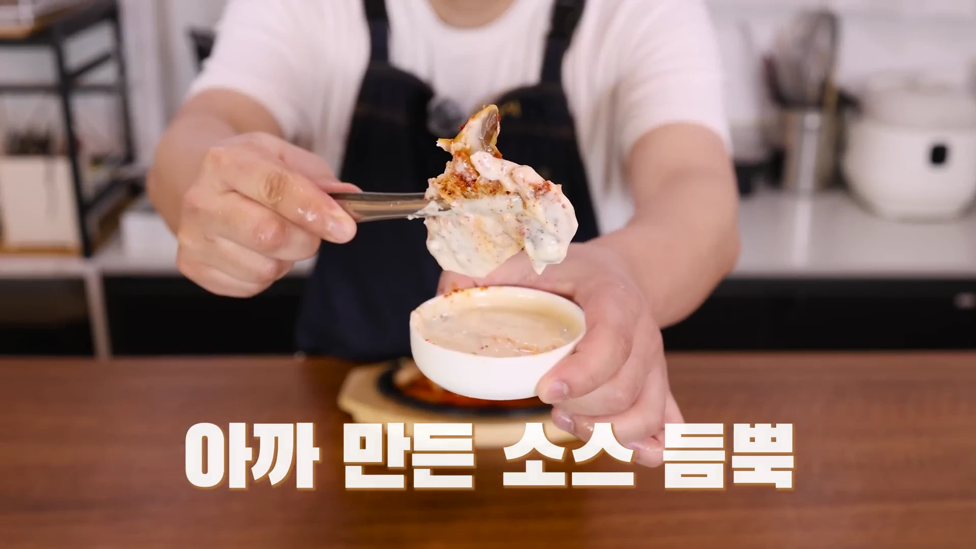 앞치마를 입은 사람이 조리된 고등어 한 점을 집게로 집어 소스 그릇에 푹 찍어 올리고 있는 모습