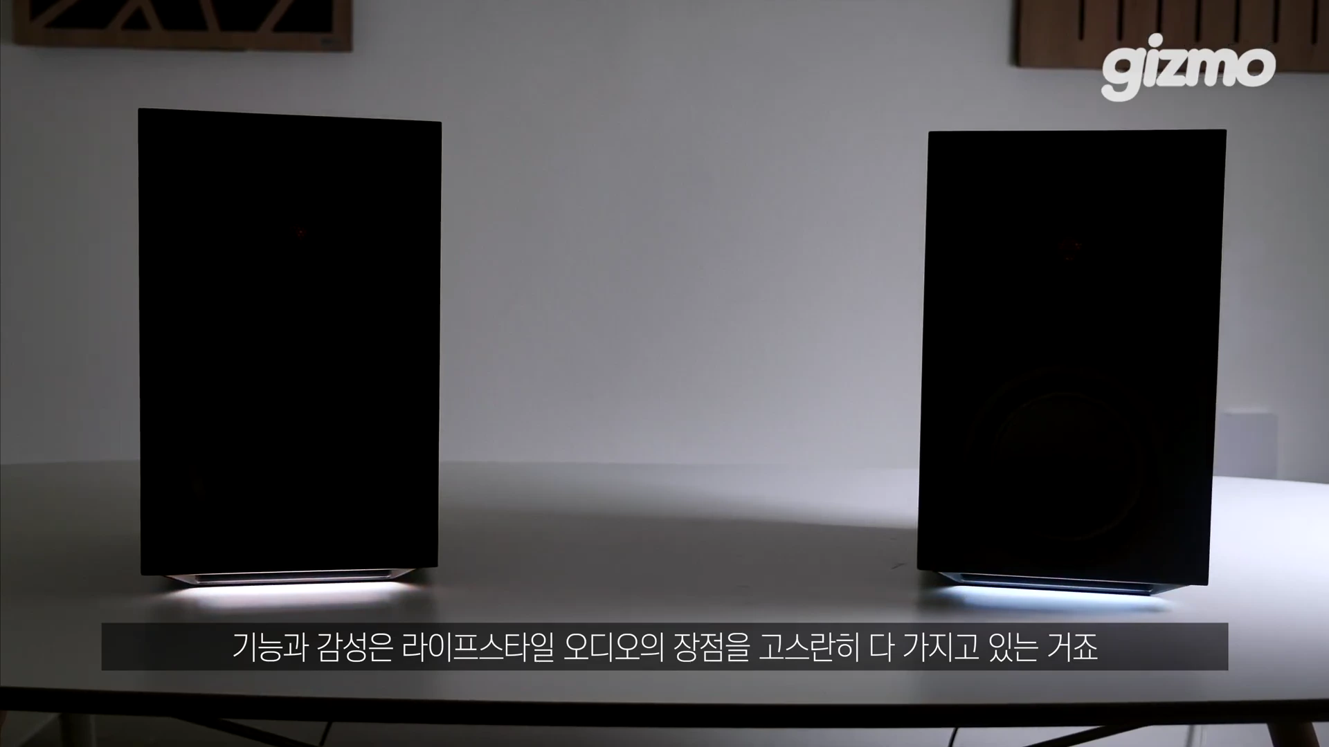 테이블 위에 놓인 한 쌍의 검은색 직사각형 스피커로, 하단에서 은은한 흰색 조명이 비치고 있는 모습입니다.