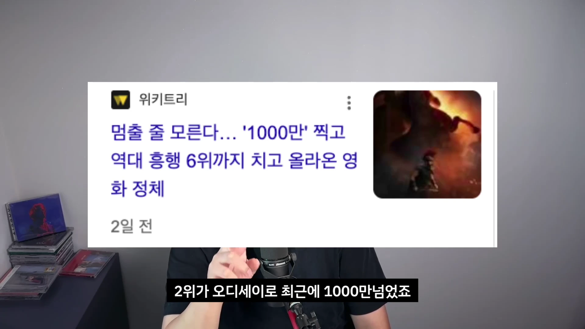 화면 중앙에 '1000만' 관객 돌파 관련 뉴스 기사 제목이 떠 있고 아래쪽에 검은색 배경의 자막이 깔린 영상 화면