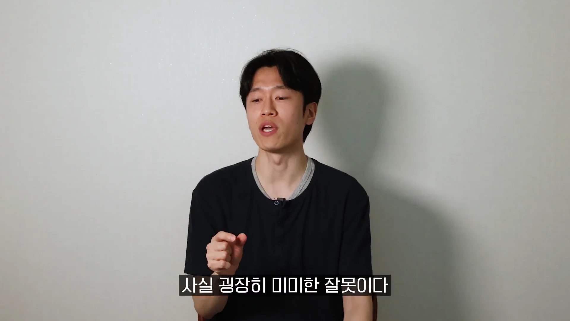 흰 벽을 배경으로 검은색 티셔츠를 입은 젊은 남성이 앉아 카메라를 보며 이야기하고 있으며, 화면 하단에는 '사실 굉장히 미미한 잘못이다'라는 자막이 표시되어 있습니다.