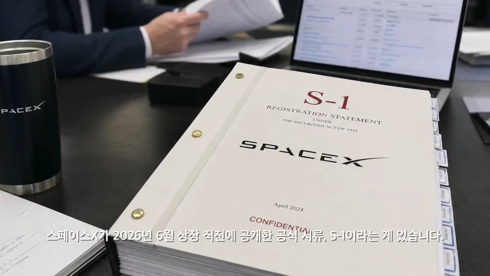 사무용 책상 위에 스페이스X 로고가 찍힌 텀블러와 함께 'S-1 Registration Statement'라고 적힌 두꺼운 서류 뭉치가 놓여 있고, 그 뒤로 노트북과 문서를 검토하는 사람의 손이 보입니다.