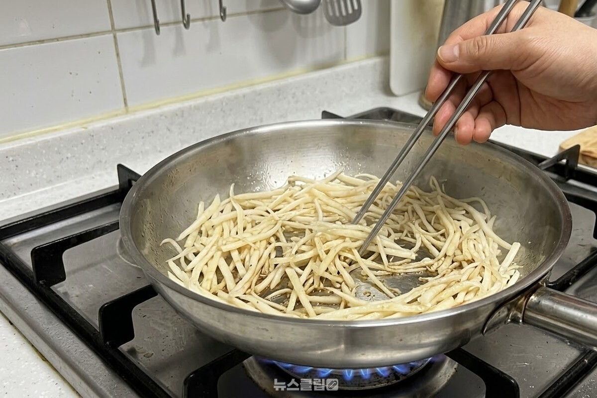 명절 상에서 물린 도라지나물을 중불에 올린 팬에 한 겹으로 펼쳐 젓가락으로 뒤집는 모습. / 기사 이해를 돕기 위한 생성형 이미지