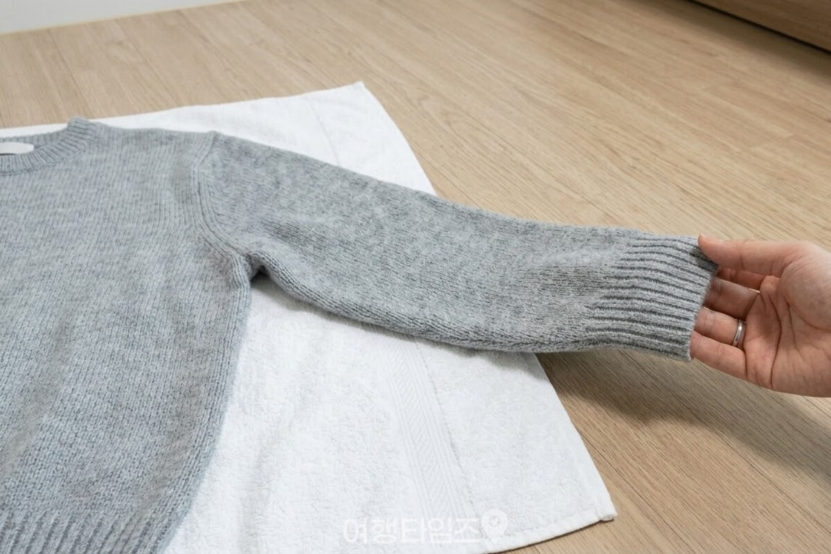 마른 수건 위에 펼쳐 놓은 니트 소매 끝을 한 손이 잡아 결을 살펴보고 있다. / 기사 이해를 돕기 위한 생성형 이미지