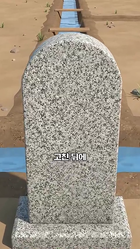 3D 애니메이션으로 구현된 봇도랑 옆에 세워진 화강암 비석 앞모습이며 화면 중앙에 '고친 뒤에'라는 한글 자막이 적혀 있습니다.