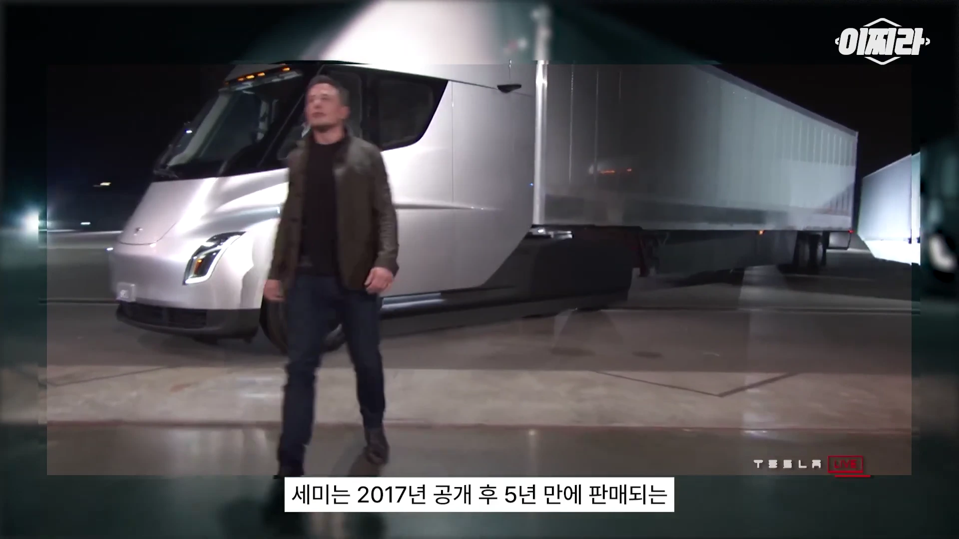 테슬라 세미 트럭이 야간에 세워진 모습 앞에 한 남성이 걷고 있는 모습이 담긴 비디오 프레임입니다.